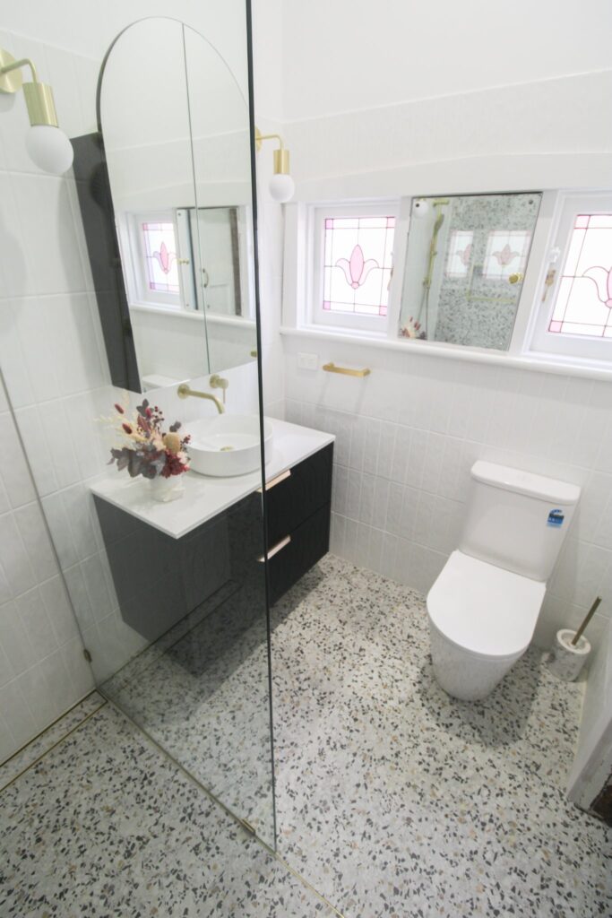 after-bathroom-renovation-floating-vanity-glass-door-gold-fixtures-small-mirror